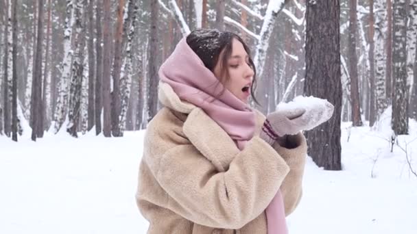 Happy young woman in eco fur coat in the winter forest blowing on show from hands. Winter outdoor activity - Imágenes, Vídeo