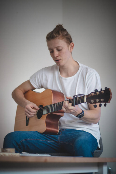 若いブロンドの少年は新しいスキルを学ぼうとしており、それはアコースティックギターである楽器を演奏しています。ギターの喉を歌い手を動かす. - 写真・画像