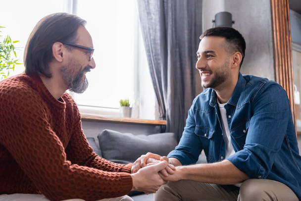 happy interracial father and son holding hands while talking at home - Foto, immagini