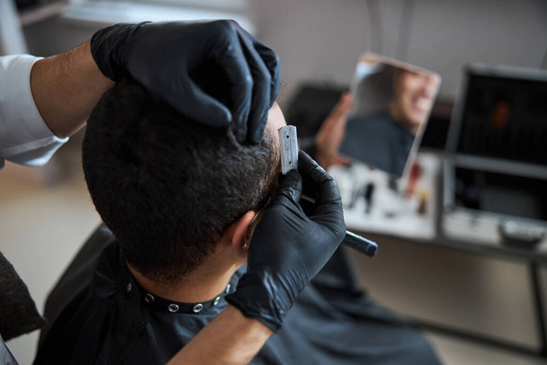 aseado hombre en negro peignoir consiguiendo peluquería en salón de belleza - Foto, imagen