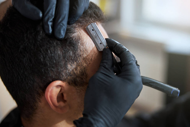 Wspaniały mężczyzna spędza czas w salonie fryzjerskim, podczas gdy stylista włosów robi fryzurę ostrzyżoną maszynką do golenia - Zdjęcie, obraz