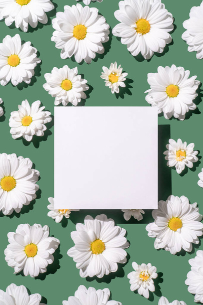 Λευκά λουλούδια μαργαρίτα σε πράσινο φόντο με λευκή χάρτινη σημείωση. Φωτεινό φως, αντίγραφο χώρου. - Φωτογραφία, εικόνα