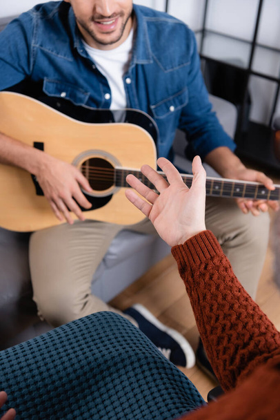 περικοπή άποψη των ατόμων με ειδικές ανάγκες δείχνοντας με το χέρι κοντά στο γιο παίζει κιθάρα σε θολή φόντο - Φωτογραφία, εικόνα