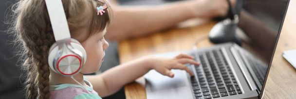 Bambina siede al computer portatile in cuffia con microfono accanto all'uomo - Foto, immagini