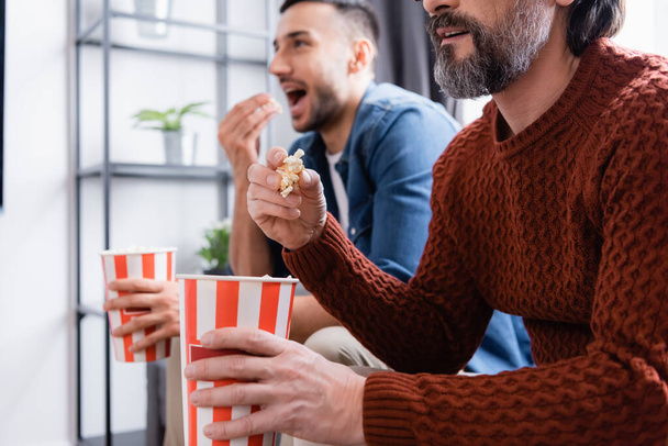 interracial father and son watching tv while eating popcorn at home, blurred background - Photo, Image