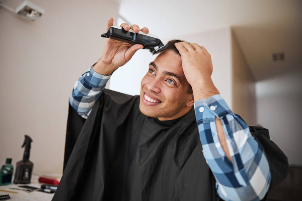 Hombre seguro de sí mismo con el pelo oscuro utilizando la máquina moderna haciendo un corte de pelo en la habitación en el interior - Foto, imagen