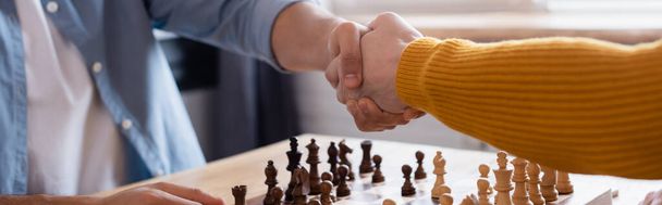 cropped view of father and son shaking hands near chessboard on blurred background, banner - Photo, Image