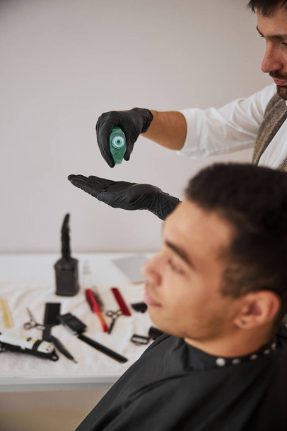 Barbiere spremitura spray su braccio mentre in piedi vicino al cliente nel salone di bellezza - Foto, immagini