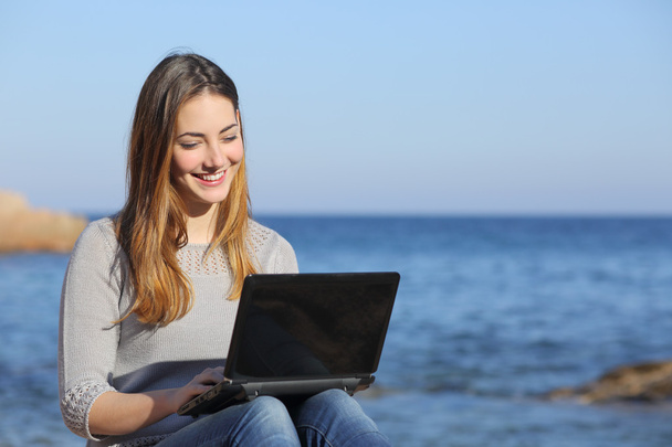 Happy teenager girl browsing social media on the beach - Фото, изображение