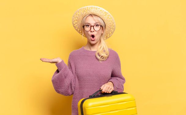 blonde woman looking surprised and shocked, with jaw dropped holding an object with an open hand on the side - Fotoğraf, Görsel