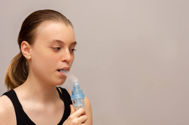 adolescente con asma e allergie fa l'inalazione con un medicinale attraverso un nebulizzatore tra le mani su uno sfondo grigio - Foto, immagini