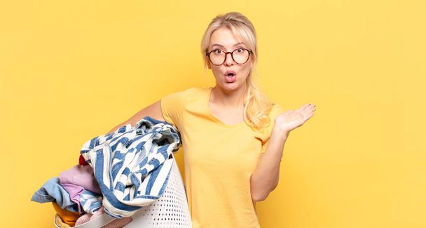 blonde woman looking surprised and shocked, with jaw dropped holding an object with an open hand on the side - Foto, imagen
