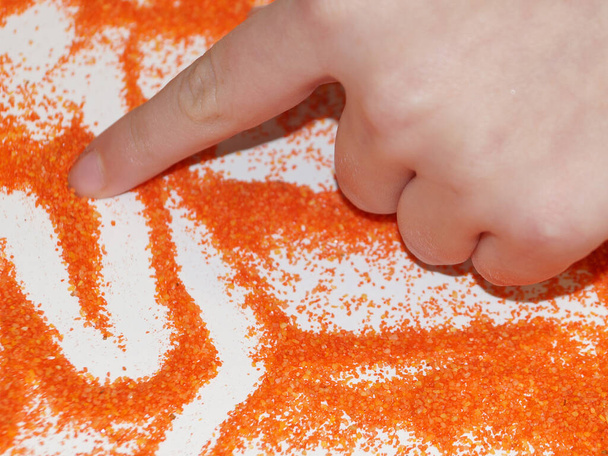 αμμοθεραπεία, παιδικό χέρι αντλεί από την πορτοκαλί κινητική άμμο. - Φωτογραφία, εικόνα