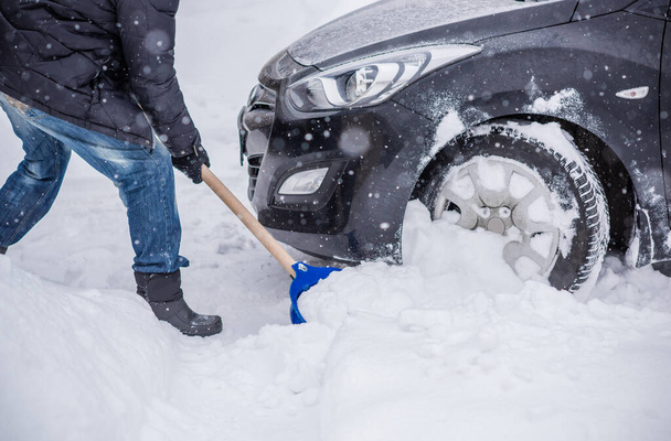 Winter, mensen en auto probleem concept. Een man probeert de auto te duwen, vast in de sneeuw. Wederzijdse hulp. Winterprobleem. transport, winter en voertuig concept - close-up van de mens duwen auto vast in de sneeuw - Foto, afbeelding