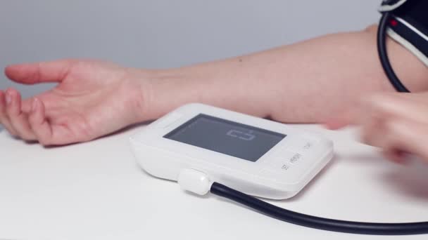Взрослая или пожилая женщина измеряет артериальное давление с помощью портативного цифрового тонометра - Кадры, видео