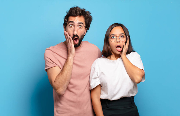 young couple feeling shocked and scared, looking terrified with open mouth and hands on cheeks - Photo, Image