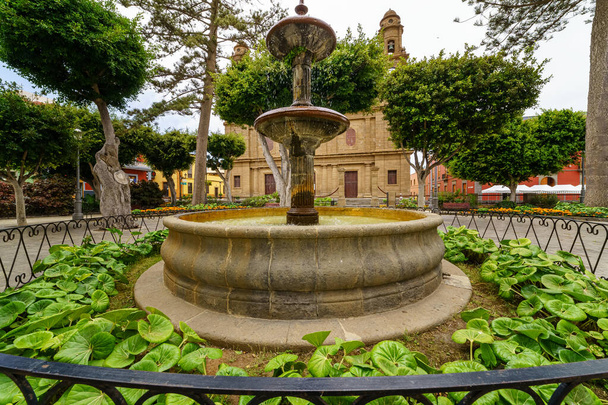 фонтан в парке на Гран-Канария рядом со старой церковью и зелеными растениями. Испания - Фото, изображение