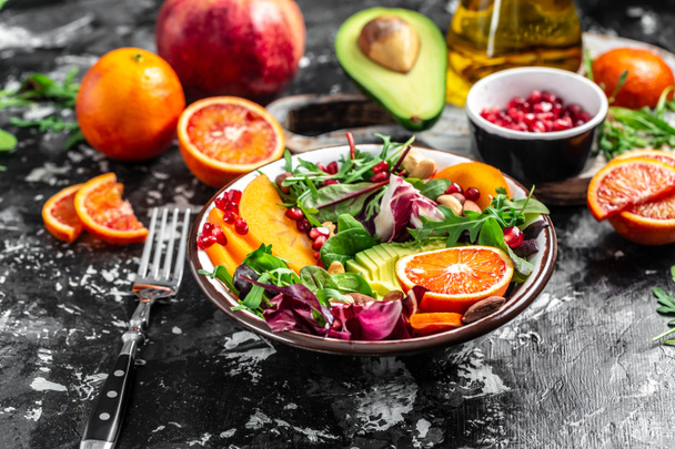 Vegan, detox Buddha bowl recipe avocado, persimmon, blood orange, nuts, spinach, arugula and pomegranate on a light background, top view - Photo, Image