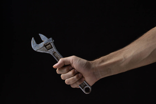 Ρυθμιζόμενο κλειδί σε μαύρο φόντο. Παλιό εργαλείο εργασίας. Το χέρι ενός άντρα κρατά ένα ρυθμιζόμενο κλειδί. - Φωτογραφία, εικόνα