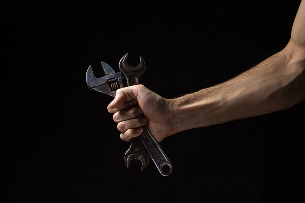 Llave y llave ajustable sobre fondo negro. Una vieja herramienta de trabajo. Una mano masculina sostiene una llave inglesa y una llave ajustable. - Foto, Imagen