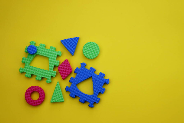 Zelené a modré puzzle kousky s pestrobarevnými geometrickými tvary na žlutém pozadí. Vzdělávací hračka  - Fotografie, Obrázek