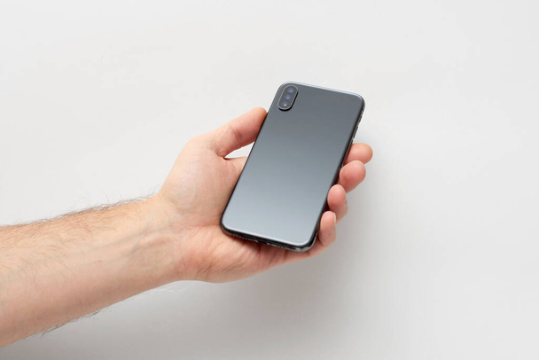 Mężczyzna trzyma czarny smartfon w ręku odizolowany na szarym tle - Zdjęcie, obraz