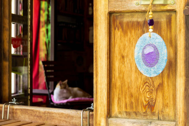 Een kwade oogkraal hangend aan het raam en een kat liggend op een stoel in de kamer - Foto, afbeelding