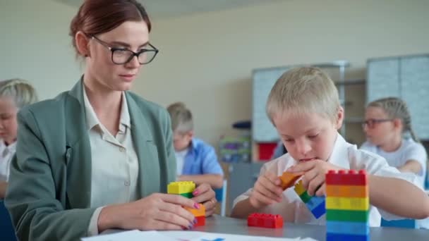 gyermek fejlődés az általános iskolában, fiú Down-szindróma játszik a konstruktor ül a tanár az asztalnál az óra alatt - Felvétel, videó