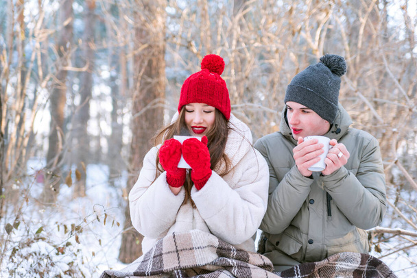 Le jeune couple pique-niquait dans le parc en hiver. Les amoureux boivent du thé en forêt. - Photo, image