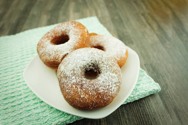 Donuts sprinkled with powdered sugar on a plate. Powdered sugar donuts with copy space - Photo, Image