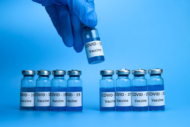 El médico sostiene una vacuna contra el coronavirus en la mano sobre un fondo azul. El concepto de la lucha contra la pandemia de ncov COVID-19 - Foto, imagen