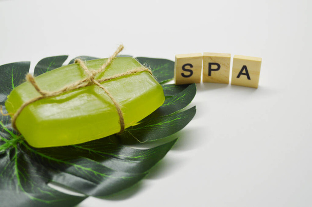 Πράσινο σαπούνι δεμένο με σχοινί βρίσκεται σε λευκό φόντο πάνω σε ένα πράσινο φύλλο φοίνικα. λέξη Spa από ξύλινα γράμματα - Φωτογραφία, εικόνα