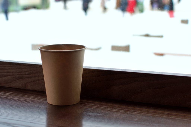 taza de papel con café en la mesa dentro de una cafetería en el fondo borroso de la calle nevada - Foto, Imagen