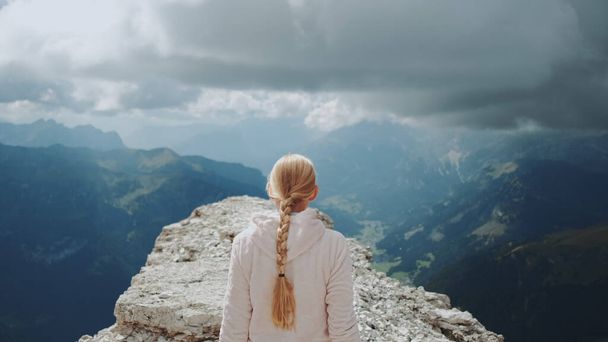 Πίσω όψη της ξανθιάς γυναίκας που περπατάει στην κορυφή του βουνού κάτω από τα σύννεφα - Φωτογραφία, εικόνα