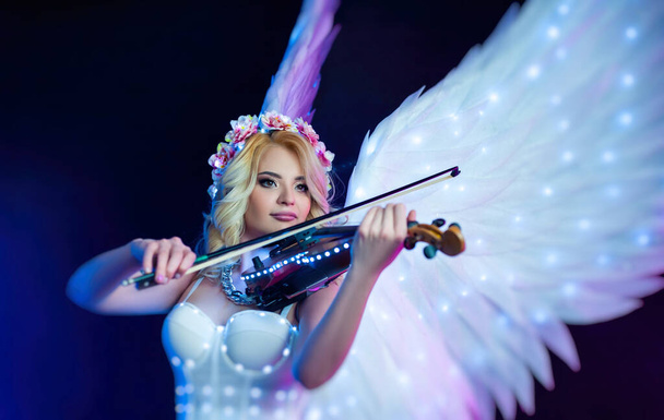 жінки з ангельськими крилами грають на скрипці в неоновому світлі
 - Фото, зображення
