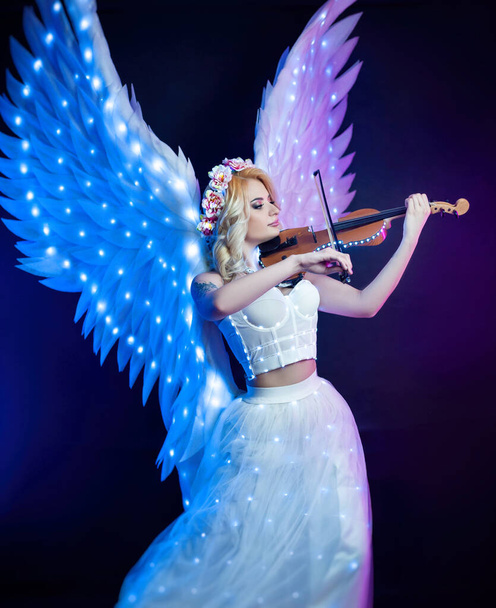 women with angel wings playing violin in neon light - Photo, Image