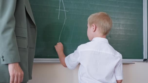 зіниця з синдромом Даунса стоїть з учителем на дошці і пише листи з білою крейдою в класі, хлопчик радіє успіху в початковій школі
 - Кадри, відео