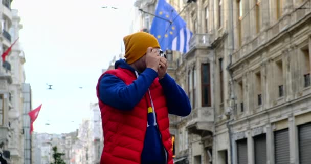 turista em um colete vermelho caminha por Salzburgo e tira uma foto com uma câmera de filme - Filmagem, Vídeo