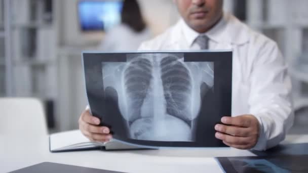 Especialista en pulmón masculino de Oriente Medio con abrigo blanco sentado en el escritorio mirando las inyecciones de rayos X en el pecho - Metraje, vídeo