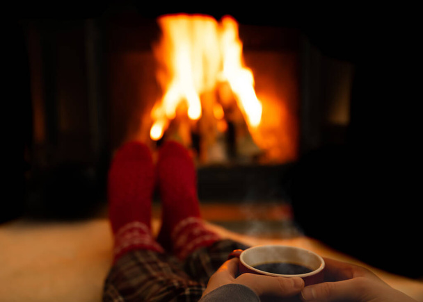 Hands holding a steaming warm cup of coffee while resting by a fireplace on a cold winters evening. High quality photo - Photo, Image