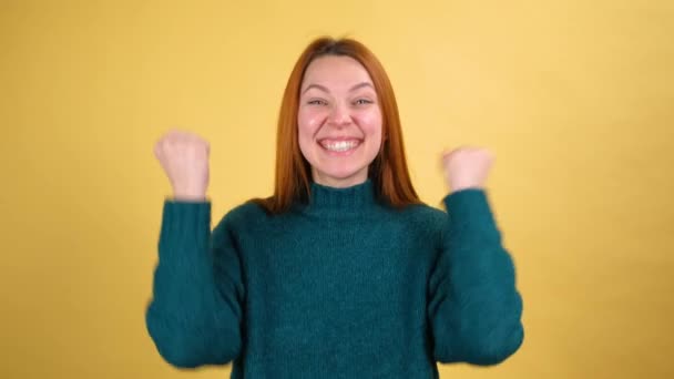 Chica americana en suéteres verdes haciendo gesto ganador decir Sí aislado sobre fondo naranja en el estudio. Gente emociones sinceras, concepto de estilo de vida. Apretando puños como ganador - Metraje, vídeo