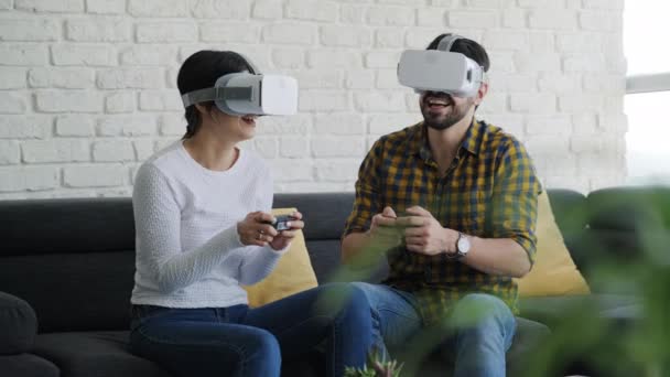 Jeune couple jouant jeu de réalité virtuelle avec des lunettes à la maison. Des gens heureux utilisant un casque VR pour les jeux en ligne. Homme et femme souriant, appréciant la technologie de divertissement domestique - Séquence, vidéo