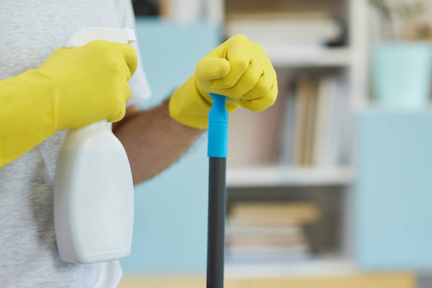 Bezpieczny i czysty. Zbliżenie ujęcia profesjonalnego męskiego czyściciela noszącego rękawiczki, trzymającego detergent natryskowy i mop podczas przygotowywania się do czyszczenia kuchni - Zdjęcie, obraz