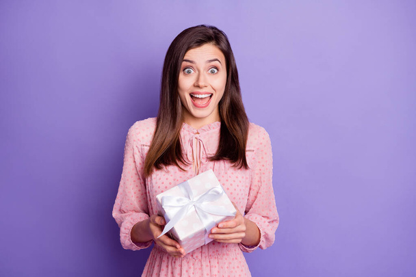 Portrait of attractive amazed cheerful girl holding in hands white giftbox isolated over bright violet color background - Photo, Image