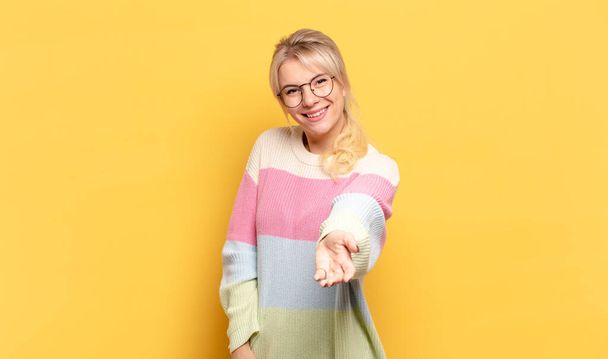 blonde woman smiling, looking happy, confident and friendly, offering a handshake to close a deal, cooperating - 写真・画像