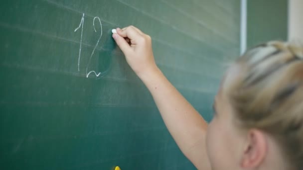 math lesson, schoolgirl at blackboard writes numbers with white chalk in classroom at elementary school - Footage, Video