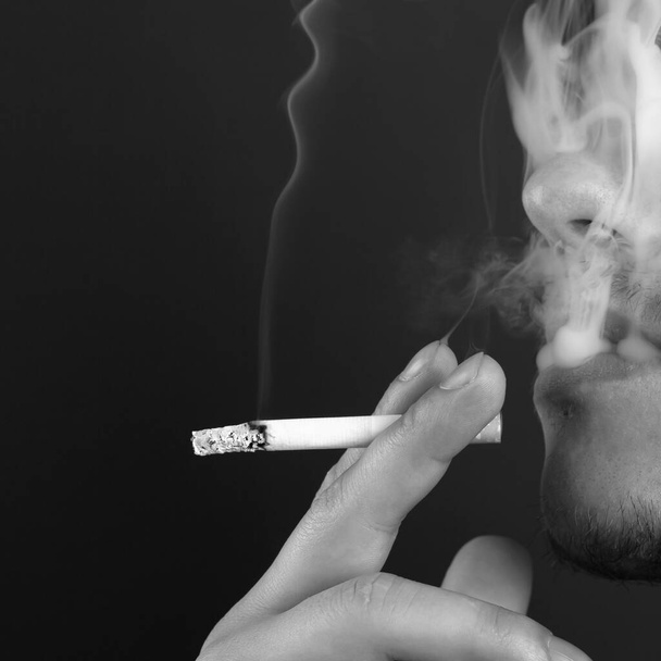homme fume une cigarette en fumée blanche sur un fond sombre - Photo, image