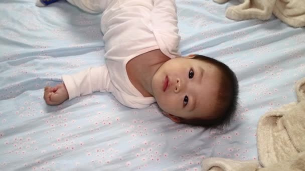 Asyalı Çinli bir çocuğun beyaz uyku tulumuyla yatakta yattığı yerel yaşam tarzı görüntüler. - Video, Çekim