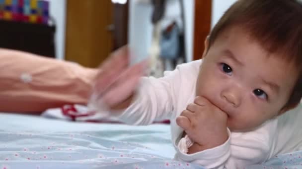Porträt eines 8 Monate alten asiatischen chinesischen Jungen, der auf dem Bauch im Bett liegt und Finger lutscht. - Filmmaterial, Video