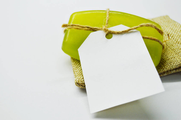 Πράσινο σαπούνι δεμένο με σχοινί με ετικέτα βρίσκεται σε λευκό φόντο σε σακούλα γιούτας. - Φωτογραφία, εικόνα